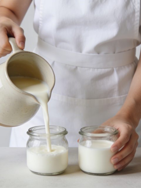 Femme versant lait chaud dans petits pots en verre