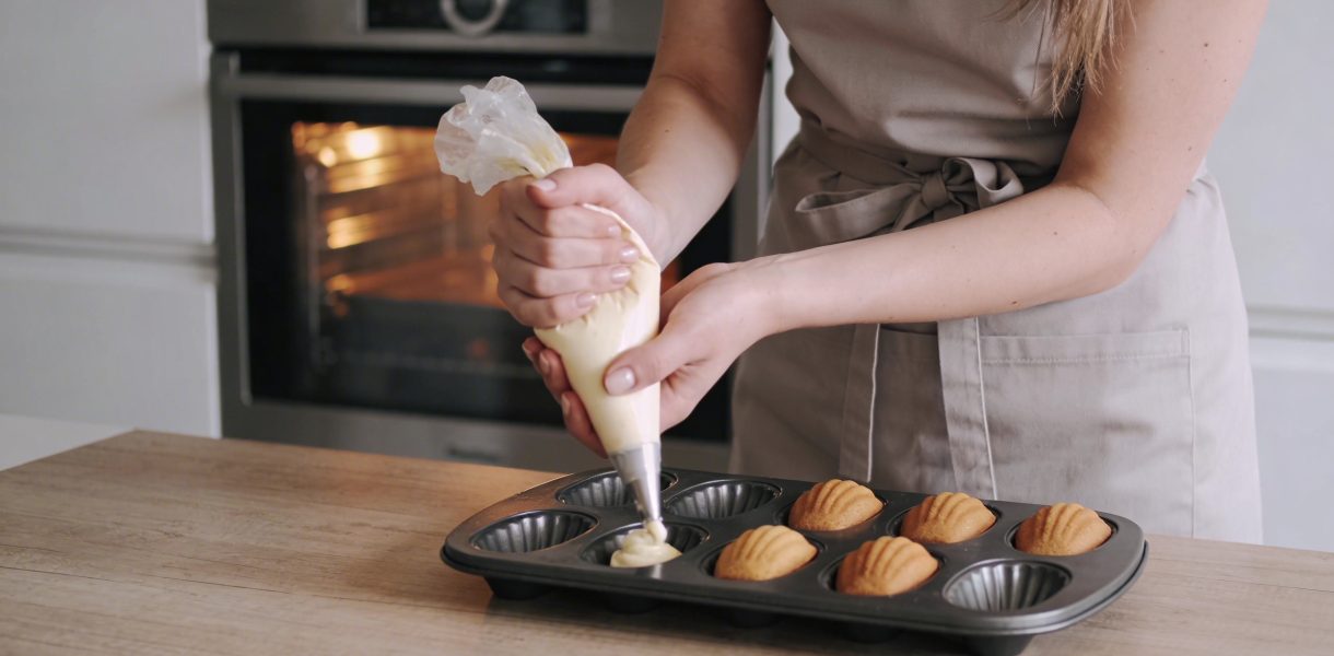 Jeune femme cuisine des madeleines devant son four