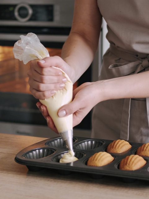 Jeune femme cuisine des madeleines devant son four