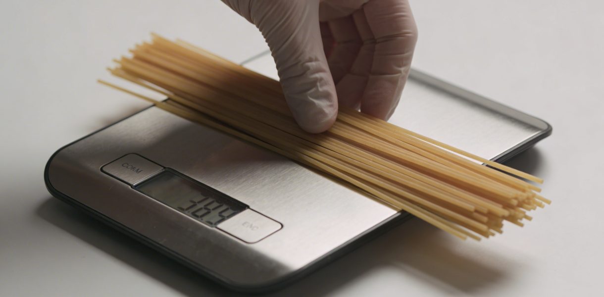 Main posant spaghetti secs sur balance de cuisine