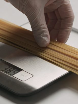 Main posant spaghetti secs sur balance de cuisine