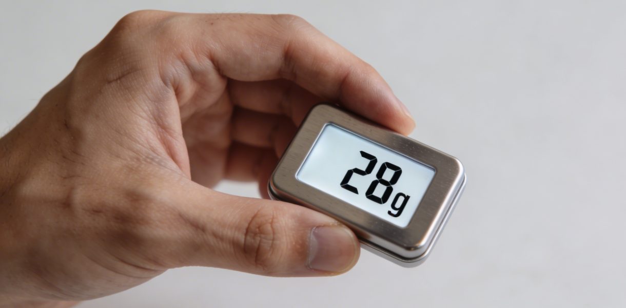 Main tenant une petite balance affichant 28 grammes