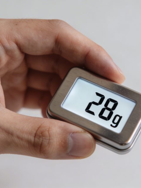 Main tenant une petite balance affichant 28 grammes