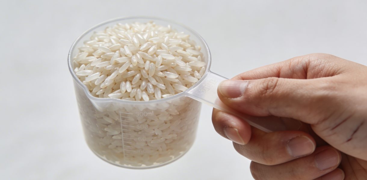 Main tenant une tasse doseuse de riz cru
