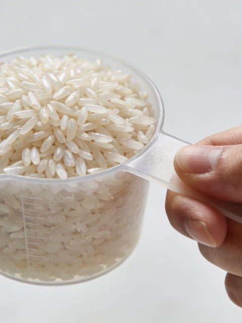 Main tenant une tasse doseuse de riz cru