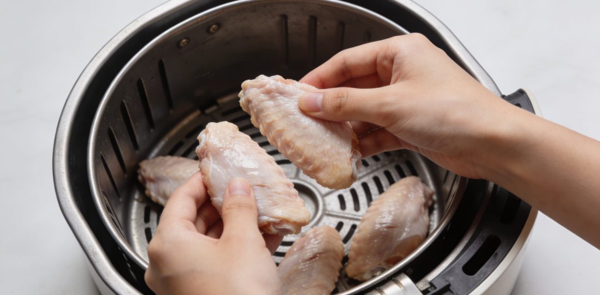 mains plaçant des aiguillettes de poulet crues dans airfryer