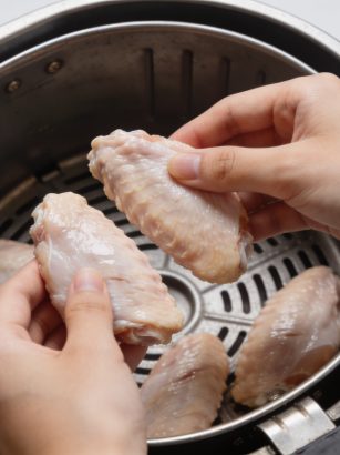 mains plaçant des aiguillettes de poulet crues dans airfryer
